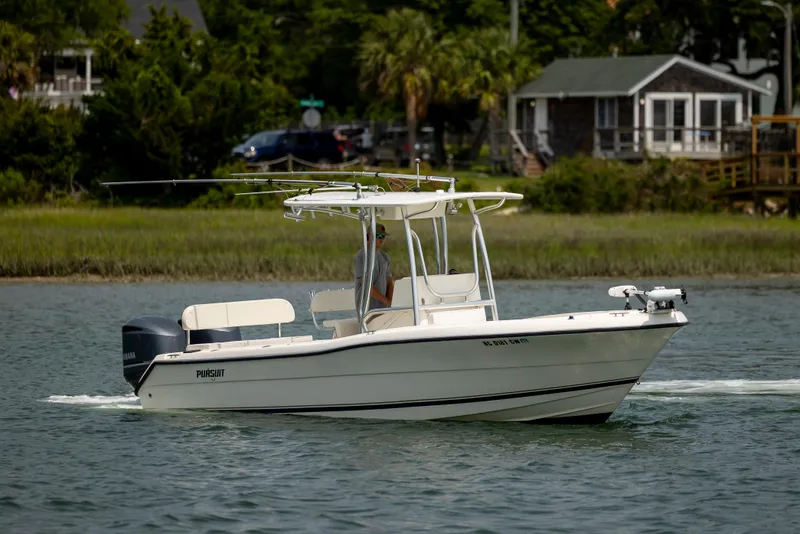 Slide: The Image of 2000 Pursuit 2470 Center Console boat cruising on a calm lake near a cottage. - 2