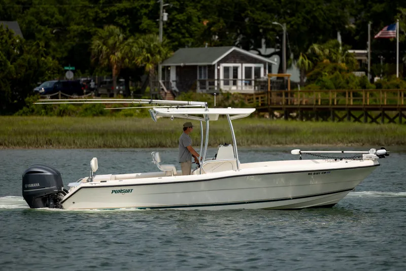 Slide: The Image of 2000 Pursuit 2470 Center Console boat cruising on a calm waterway near a coastal home. - 3