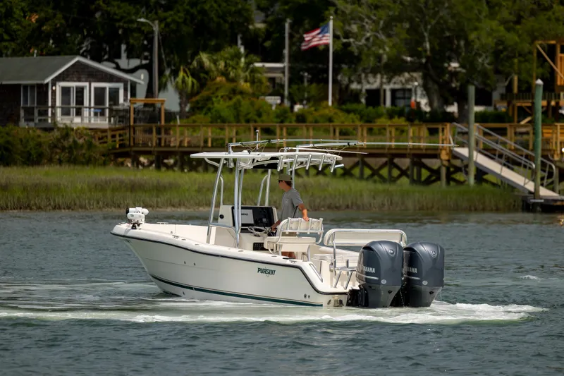 Slide: The Image of 2000 Pursuit 2470 Center Console boat cruising on a calm river near a wooden dock. - 5