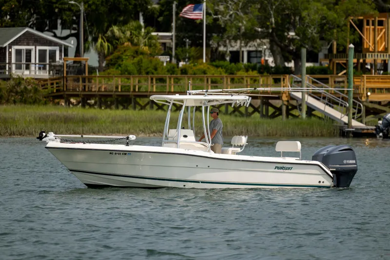Slide: The Image of 2000 Pursuit 2470 Center Console boat on water near a wooden dock and greenery. - 8