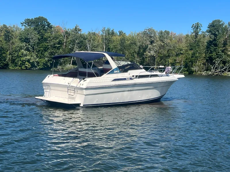 Slide: The Image of 1988 Silverton 34X Express boat cruising on a calm lake with forested shoreline. - 2