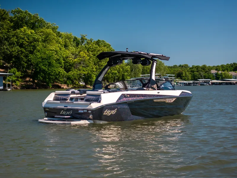 Slide: The Image of 2025 Tigé Ultré 23ZX boat on a serene lake with lush green trees. - 5