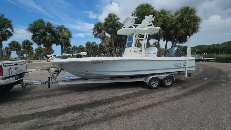 Slide: The Image of 2020 Robalo 246 Cayman boat on trailer, parked near palm trees under a cloudy sky. - 13