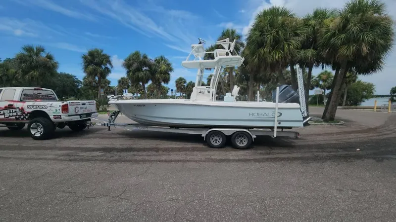 Slide: The Image of 2020 Robalo 246 Cayman boat on trailer, parked near palm trees under a blue sky. - 14