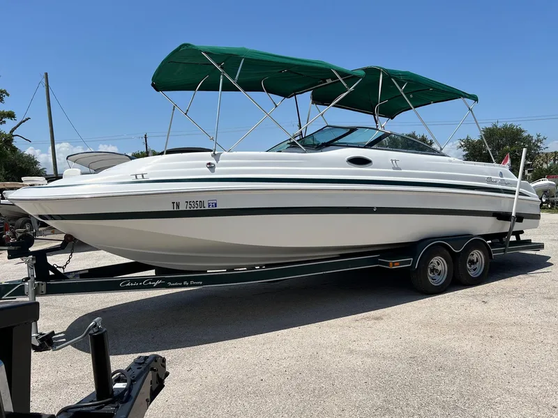 Slide: The Image of 2000 Chris-Craft 260DB boat with green canopy on a trailer, parked outdoors. - 0