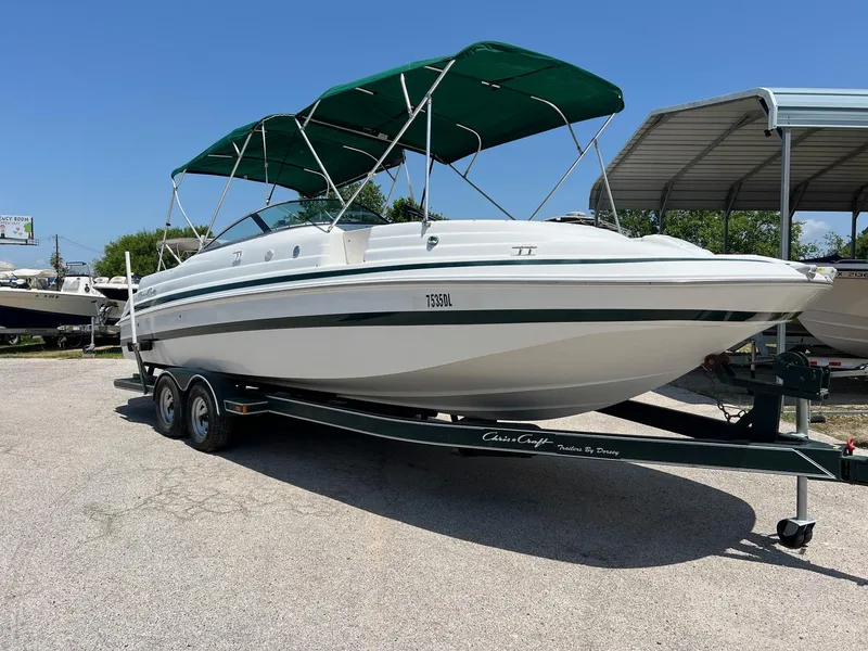 Slide: The Image of 2000 Chris-Craft 260DB boat with green canopy on a trailer, parked outdoors. - 2