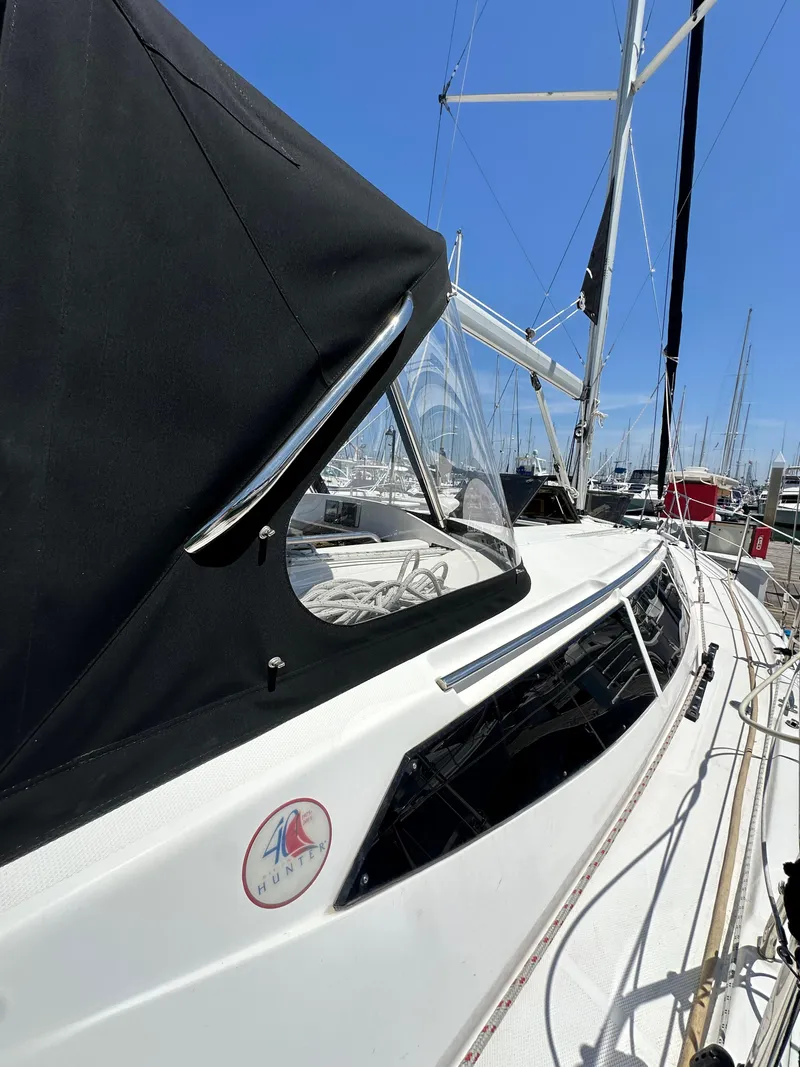 Slide: The Image of 2013 Hunter 33 sailboat with black canopy, docked in marina under clear blue sky. - 9