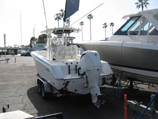 Slide: The Image of 2023 Edgewater 245CC boat on trailer, parked in marina with palm trees in background. - 2