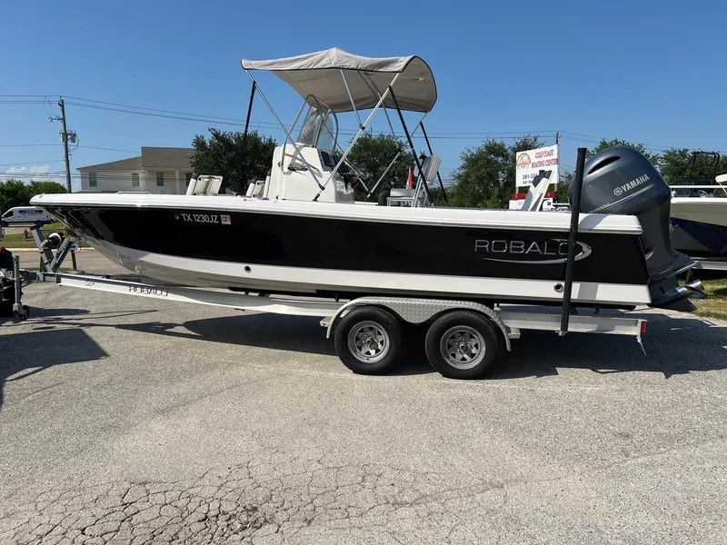 Slide: The Image of 2021 Robalo 226 Cayman boat on trailer, black and white design, parked outdoors. - 2