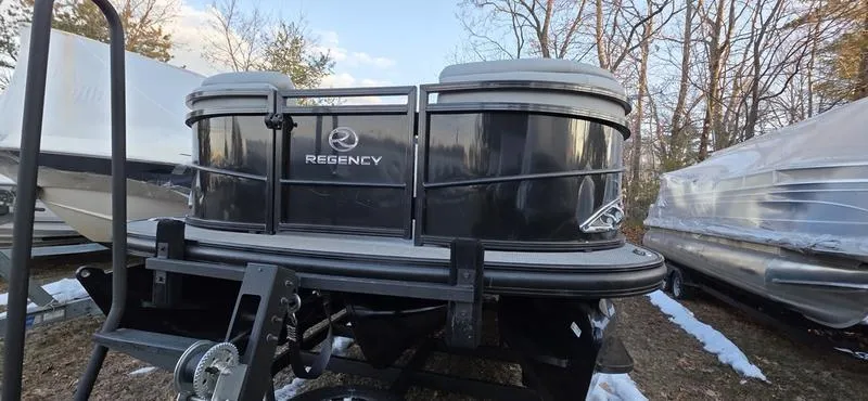 Slide: The Image of 2017 Regency 254 LE3 Sport pontoon boat, black exterior, parked outdoors in a wooded area. - 12