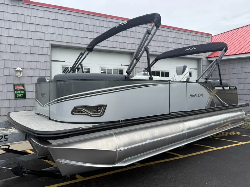 Slide: The Image of 2025 Avalon LSZ Quad Lounger 24' Tri Toon High Performance pontoon boat in parking lot. - 1