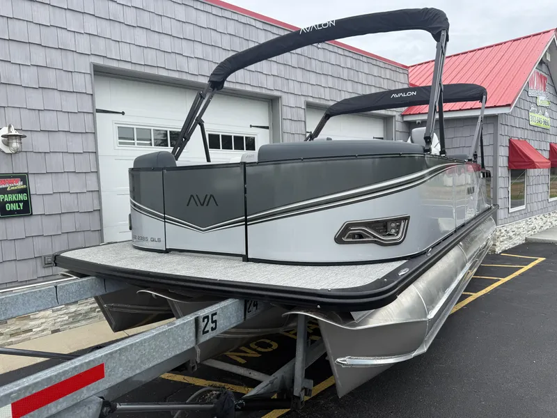 Slide: The Image of 2025 Avalon LSZ Quad Lounger 24' Tri Toon boat on trailer, parked outside a building. - 4