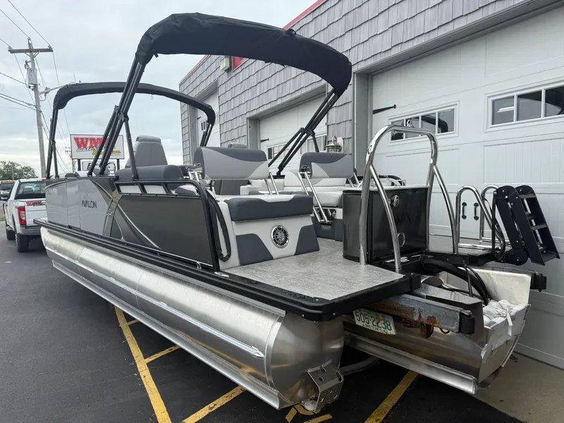 Slide: The Image of 2025 Avalon LSZ Quad Lounger 24' Tri Toon High Performance boat parked near a garage. - 6