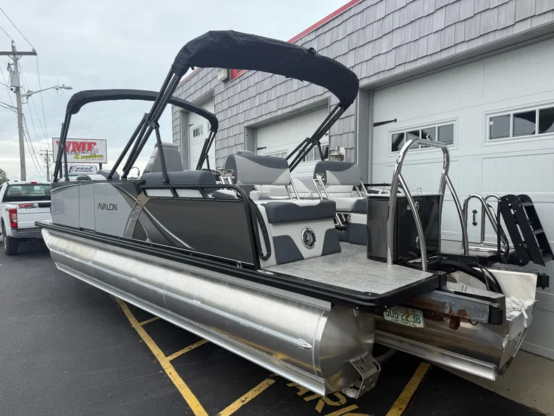 Slide: The Image of 2025 Avalon LSZ Quad Lounger 24' Tri Toon High Performance boat parked near a garage. - 7