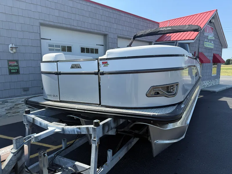 Slide: The Image of 2025 Avalon Catalina Quad Lounger Shift Windshield boat on trailer, parked outside a building. - 4