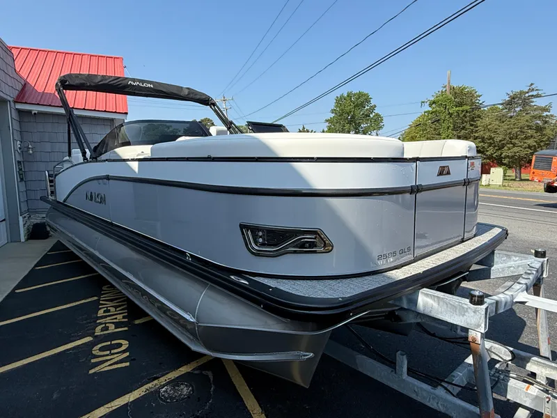Slide: The Image of 2025 Avalon Catalina Quad Lounger Shift Windshield boat on trailer, parked outdoors. - 7