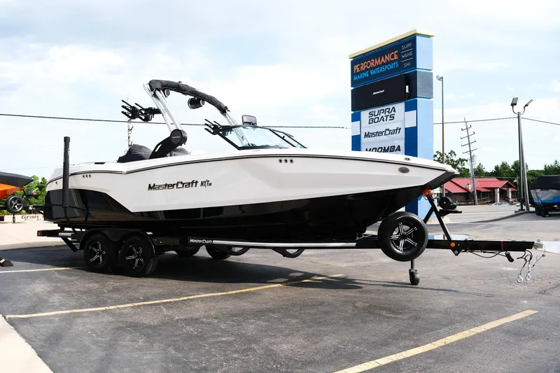 Slide: The Image of 2025 MasterCraft NXT24 boat on trailer in parking lot, dealership sign in background. - 10