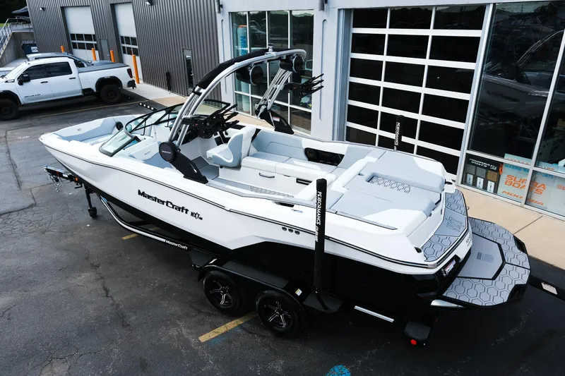 Slide: The Image of 2025 MasterCraft NXT24 boat on trailer, parked outside a modern building. - 4