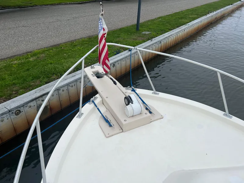 Slide: The Image of 1989 Mako 250 Cuddy Cabin boat bow with American flag, docked by grassy shoreline. - 3