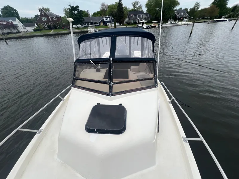 Slide: The Image of 1989 Mako 250 Cuddy Cabin boat docked on calm water, surrounded by houses. - 5