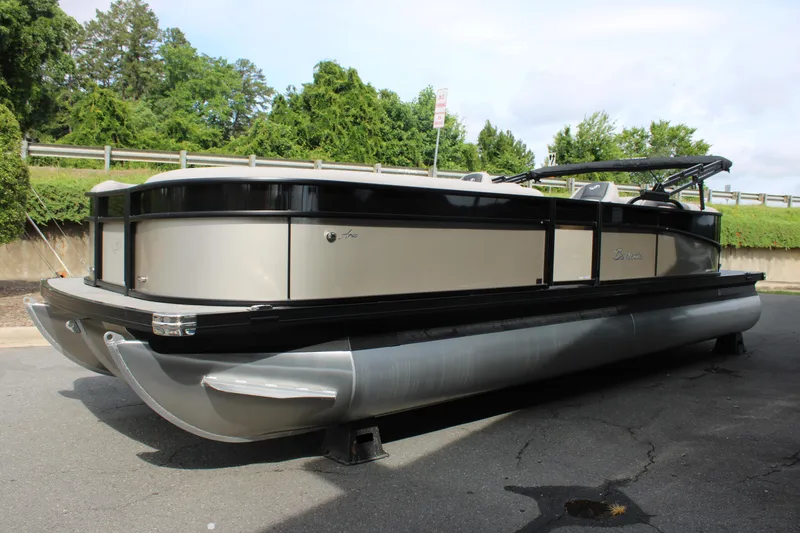 Slide: The Image of 2025 Barletta Aria 24QC pontoon boat parked on pavement, surrounded by greenery. - 13