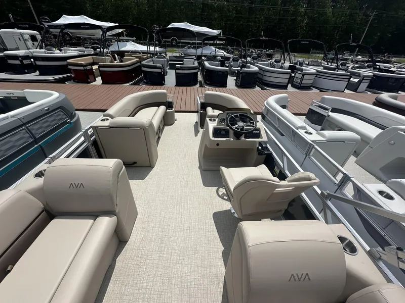 Slide: The Image of 2025 Avalon VLS pontoon boat interior with beige seating, steering console, and docked boats in background. - 5
