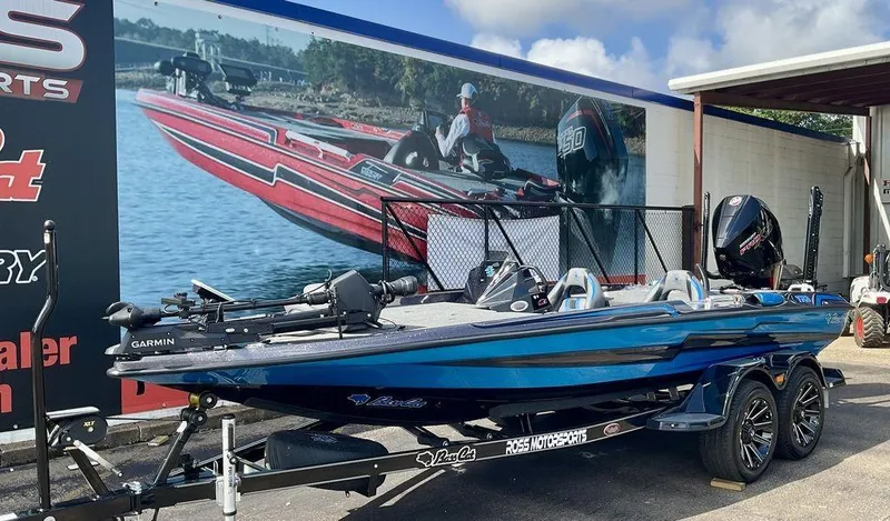 Slide: The Image of 2025 Bass Cat Eyra boat in blue, parked at dealership with promotional backdrop. - 5