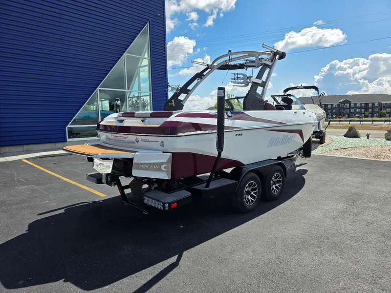 Slide: The Image of 2020 Malibu 21VLX boat on trailer, parked outside a blue building under a sunny sky. - 9