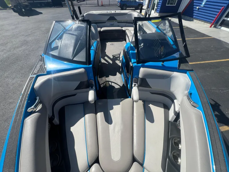Slide: The Image of 2014 Malibu W23LSV boat interior with blue and gray seating, open windshield, and cup holders. - 16