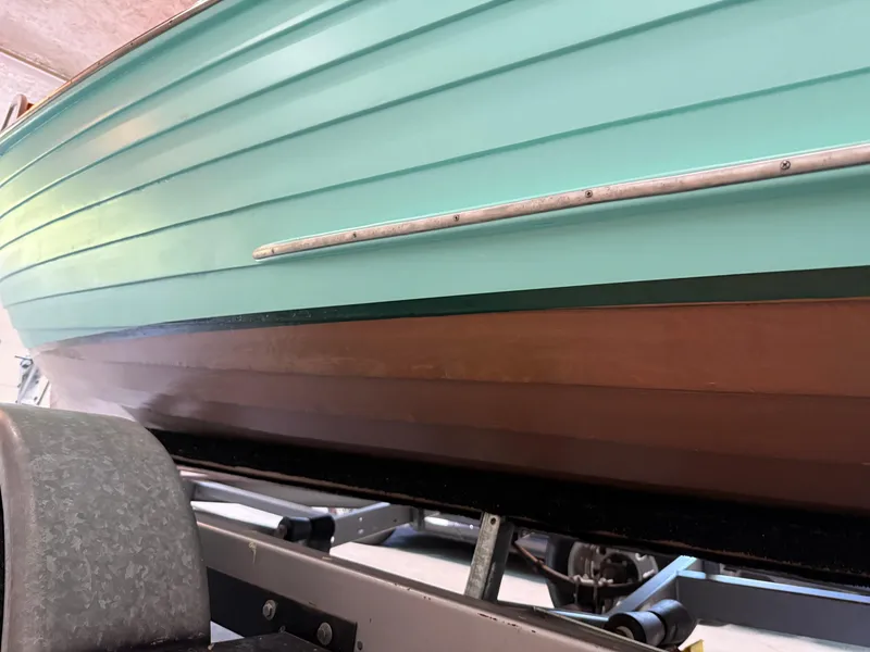 Slide: The Image of 1955 Lyman 18 Inboard boat on trailer, featuring teal and brown hull. - 15