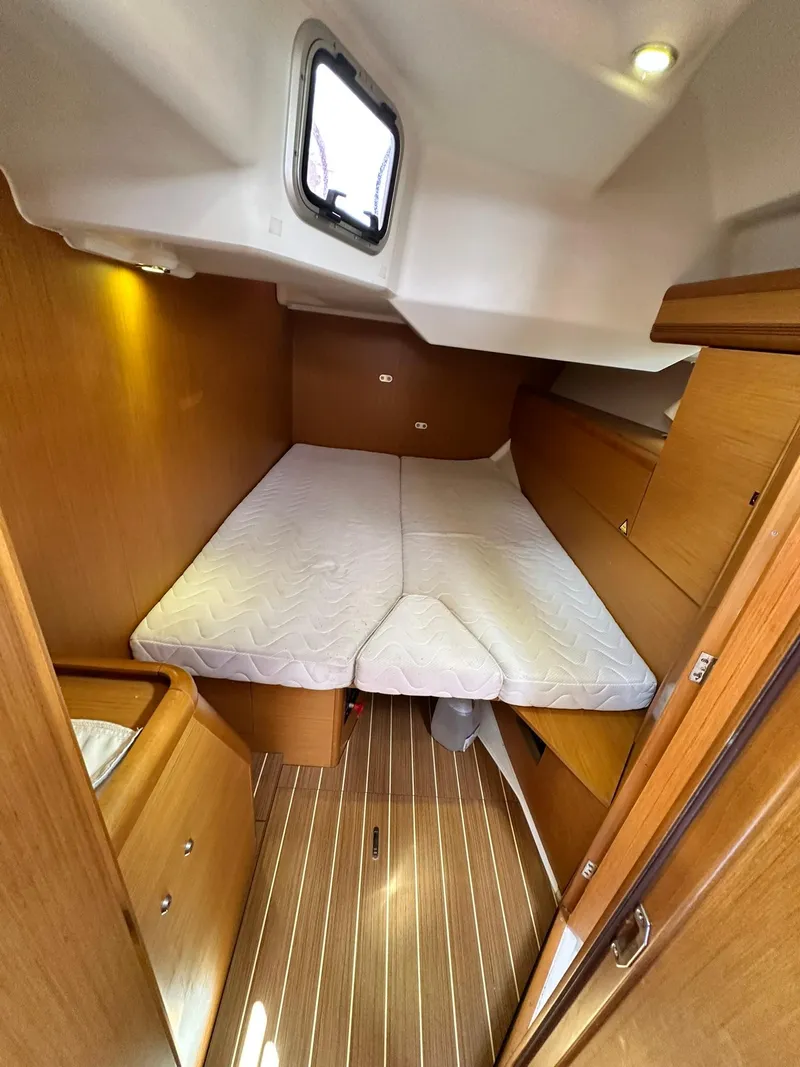 Slide: The Image of 2011 Jeanneau Sun Odyssey 45 DS cabin with bed, wooden interior, and porthole window. - 51