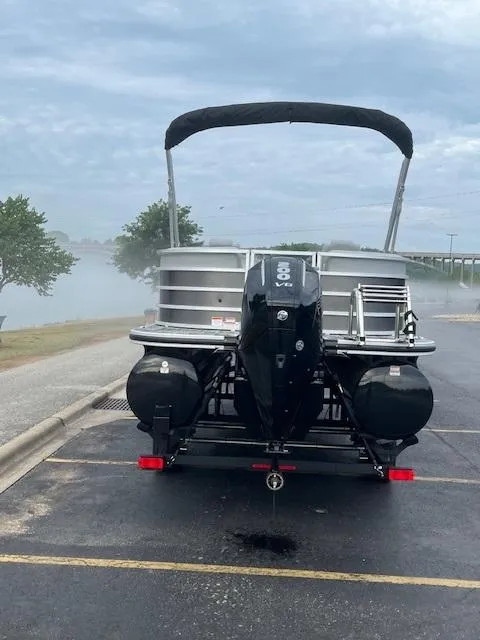 Slide: The Image of 2025 Ranger Reata 243C pontoon boat on trailer, parked in a lot near water. - 3