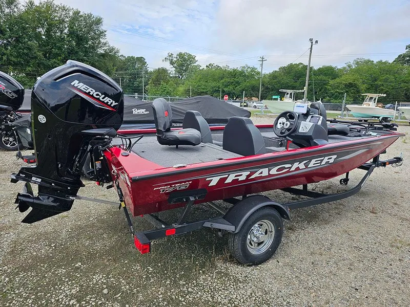 Slide: The Image of 2025 Tracker Pro Team 175 boat with Mercury engine, parked on gravel, surrounded by trees. - 3