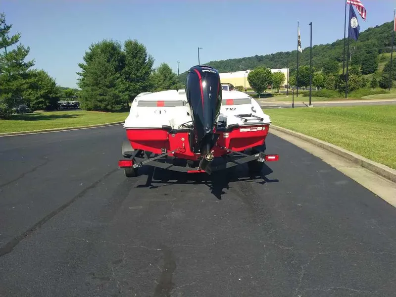 Slide: The Image of 2025 Tahoe T18 boat on trailer, parked on asphalt road with green trees and flags in background. - 3