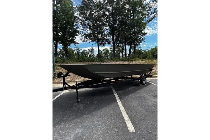 The Image of 2025 Tracker Grizzly 2072 Utility boat on trailer in parking lot, surrounded by trees. - 0
