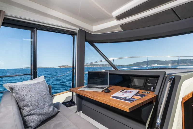 Slide: The Image of 2025 Marex 440 Gourmet Cruiser interior with ocean view, featuring a laptop and comfortable seating. - 46