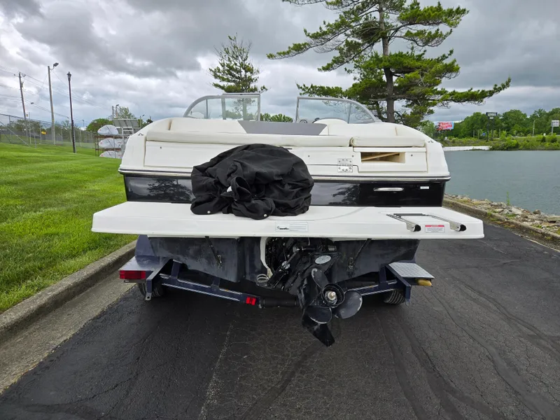 Slide: The Image of 2015 Bayliner 642 Overnighter boat on trailer, parked near a lake with overcast skies. - 2