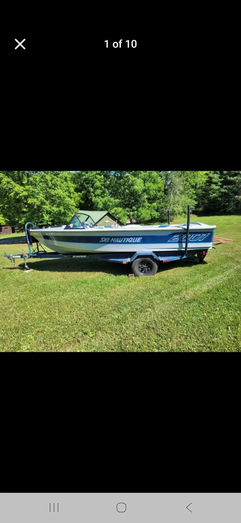 Slide: The Image of 1986 Correct Craft Ski Nautique boat on trailer, parked on grass with trees in background. - 0