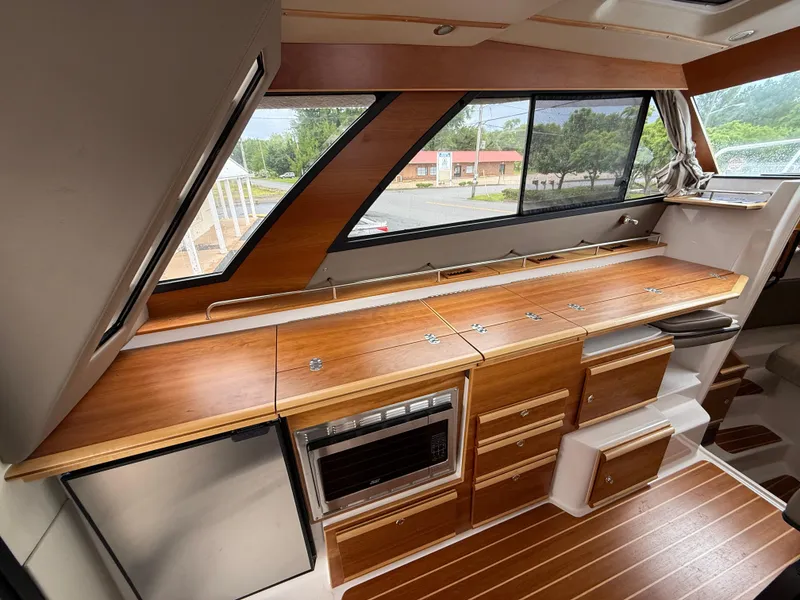 Slide: The Image of 2023 Cutwater C-32 CB interior with wood finish, featuring a kitchenette and large windows. - 19
