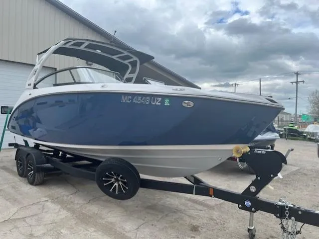 Slide: The Image of 2024 Yamaha Boats 252 S on trailer, blue and white hull, parked outdoors. - 2