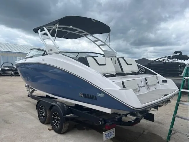 Slide: The Image of 2024 Yamaha Boats 252 S, blue and white, on trailer, under cloudy sky. - 4
