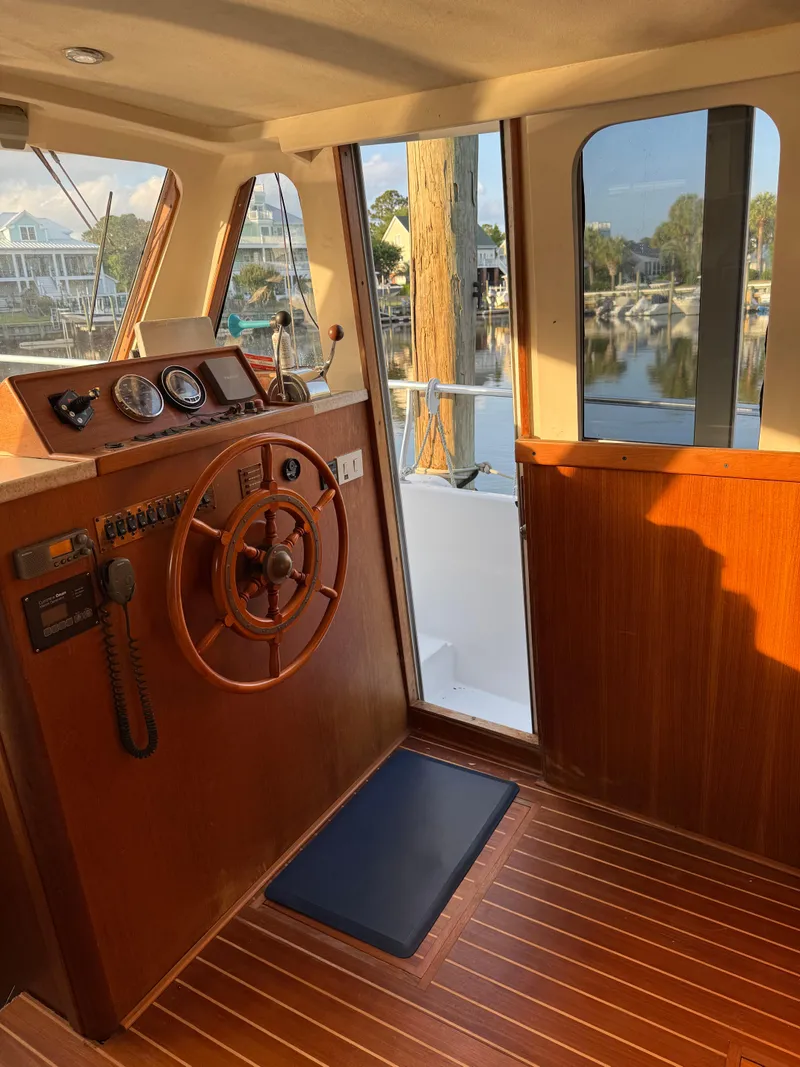 Slide: The Image of 2000 Mainship 390 Trawler helm with wooden steering wheel and scenic marina view. - 10