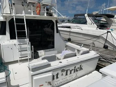 Slide: The Image of 1989 Trojan 12 Meter Convertible yacht docked, featuring a spacious deck and ladder. - 23