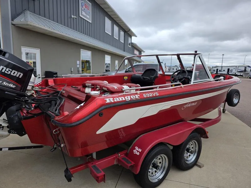 Slide: The Image of Red 1997 Ranger 692 boat on trailer, parked near a building under cloudy skies. - 5