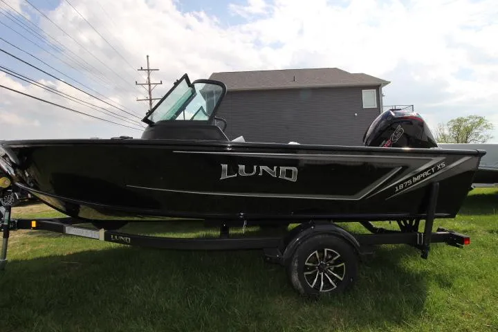 Slide: The Image of 2025 Lund 1875 Impact XS Sport boat on trailer, parked on grass. - 0