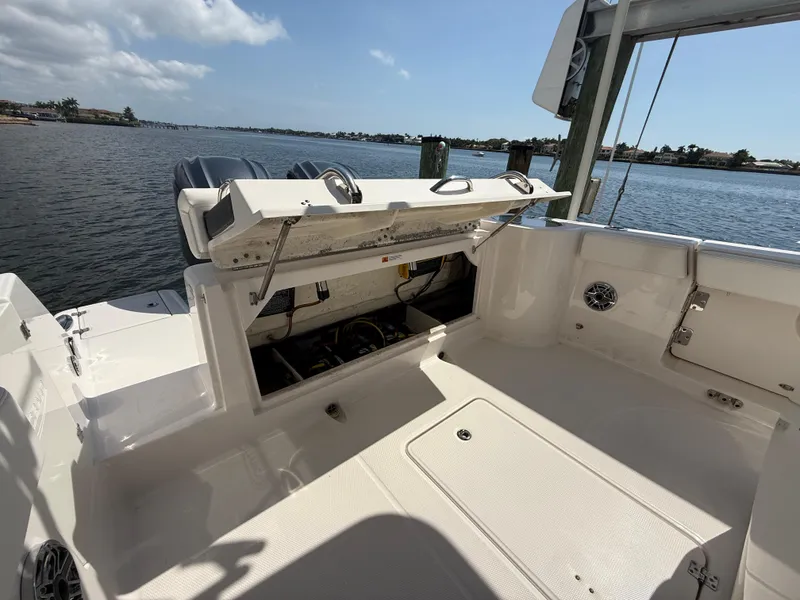 Slide: The Image of 2023 Robalo R272 Center Console boat with open storage compartment, docked by a scenic waterfront. - 19