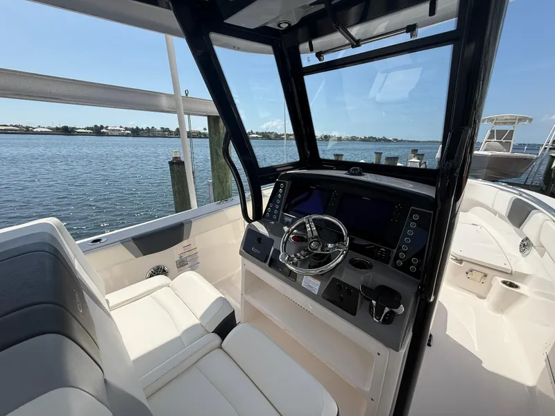 Slide: The Image of 2023 Robalo R272 Center Console boat interior with steering wheel and seating, docked by the water. - 25