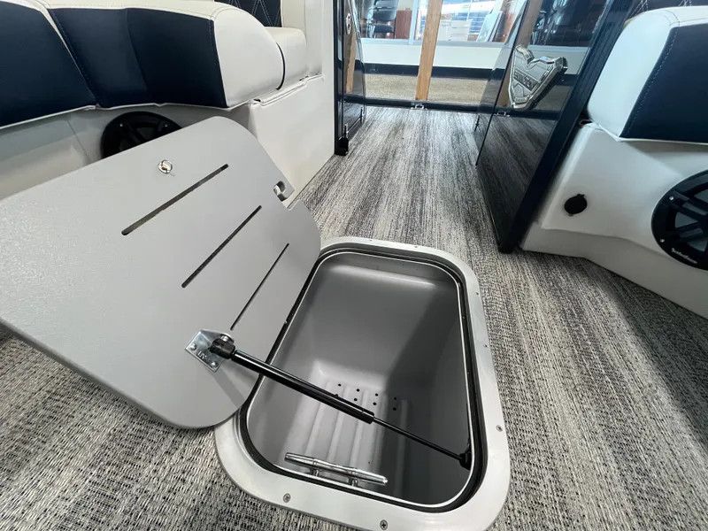 Slide: The Image of 2025 Bennington 25QXSBA boat interior with open storage compartment on carpeted floor. - 25