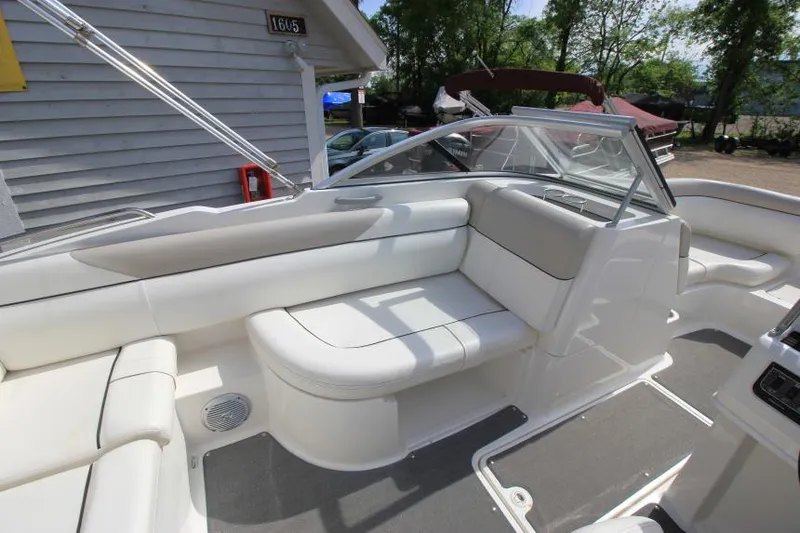 Slide: The Image of 2013 Bayliner 190 Deck Boat interior with white seating and windshield, parked outdoors. - 13