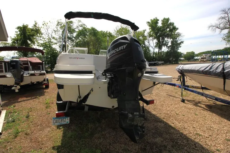Slide: The Image of 2013 Bayliner 190 Deck Boat with Mercury outboard motor, parked on gravel. - 6